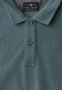 Teal polo shirt i texturerat tyg med krage, två knappar och en etikett som säger "Street One Men."