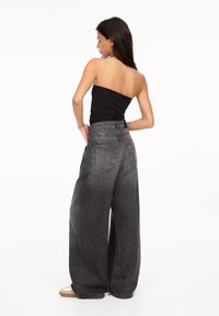 Schwarze Denim-Jeans mit weitem Bein und leicht ausgebleichtem Finish, ausgestattet mit zwei Gesäßtaschen und einer hohen Taille. Kombiniert mit einem schwarzen trägerlosen Oberteil.