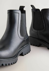 Botas Chelsea de cuero negro con paneles laterales de elastano y suelas de goma texturizadas, exhibidas desde un ángulo ligero sobre un fondo neutro.