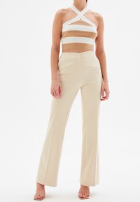 Top corto a rayas blancas y beige con tirantes cruzados y detalle de ojal, combinado con pantalones de campana beige de tejido suave.