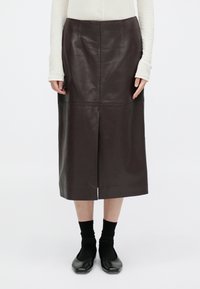 Brąskowa skórzana spódnica midi z przodu z rozcięciem, z przeszytymi panelami i gładką fakturą. Połączona z czarnymi balerinami i skarpetkami do kolan.