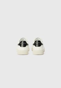 Hvite skinnsneaks med svarte semskede hælakkenter, teksturerte gummisåler, og logodetaljer bak. Rund design og polstret ankel.
