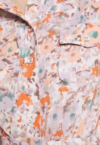 Blusa con estampado floral en colores durazno, lavanda y menta. Presenta mangas cortas, botones y un bolsillo en el lado izquierdo.