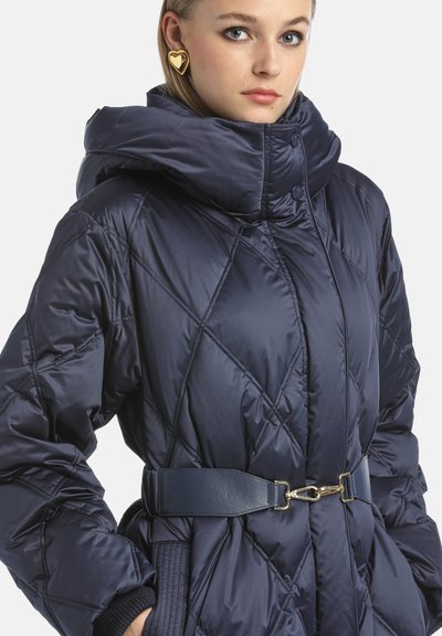 Geacă puffer navy matlasată cu guler înalt, talie strânsă evidențiată de o curea din piele și accente din metal aurit. Textură netedă și lucioasă.