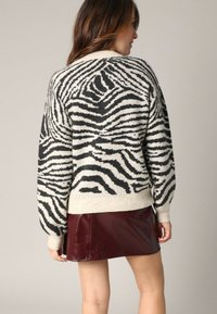 Pull en motif zèbre noir et crème, conçu en maille texturée, avec une coupe ample et des poignets côtelés, associé à une mini-jupe en cuir bourgogne.