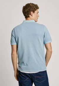 Light blue polo shirt with short sleeves, a folded collar, and a straight hem, worn with dark denim jeans.