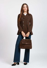 Cappotto doppiopetto marrone con grandi bottoni neri, abbinato a jeans blu a zampa d'elefante e una borsa in suede marrone scuro. Tacchi neri completano il look.
