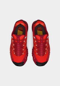 Κόκκινα αθλητικά παπούτσια με υφασμάτινο επάνω μέρος από συνθετικό υλικό, διαθέτουν ανακλαστικές λεπτομέρειες, μαλακό πάτο για απορρόφηση κραδασμών και ανθεκτική μαύρη σόλα για καλύτερη πρόσφυση.