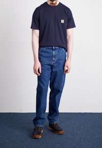 Laivastonsininen puuvillainen t-paita rintataskulla, yhdistetty vaaleansinisiin väljämallisiin farkkuihin ja ruskeisiin nyörikenkiin, joissa on paksu pohja.