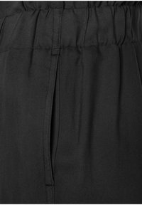 Schwarze Hose aus einem glatten Stoff, mit einem elastischen Bund und seitlichen Taschen, die über ein dezentes diagonales Textur-Detail verfügen.