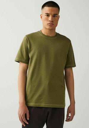 Olijfgroen katoenen t-shirt met korte mouwen, ronde hals en contrasterende stiksels. Eenvoudig, casual ontwerp zonder patronen.