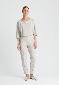 Lichtgrijze, losvallende top met een brede halslijn; bijpassende taps toelopende broek met voornaad; zilveren platte schoenen met een metallic afwerking.