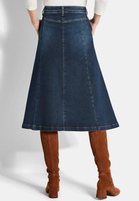 Jupe A-line en denim de coupe mi-longue, couleur bleu foncé, avec une texture lisse ; associée à des bottes en daim marron jusqu'aux genoux.