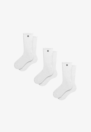 Trois paires de chaussettes blanches de type crew, chaque paire présentant un petit logo noir près du haut de la tige, disposées sur un fond blanc.