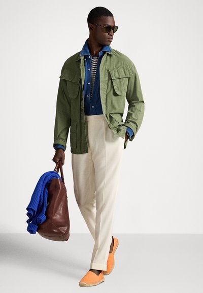 Chaki spalvos švarkas, mėlyni dryžuoti marškiniai, kreminės kelnės, oranžinės espadrilės. Ruda odinė rankinė, mėlynas megztinis užmestas ant pečių, akiniai nuo saulės.