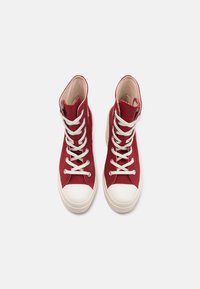 Sneaker alte rosse, materiale in tela, lacci bianchi, punta in gomma e suola color crema. Presentano dettagli cuciti sulla parte superiore.