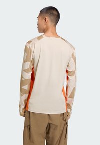 Majica dugih rukava u bež i narančastoj boji s geometrijskim uzorcima na rukavima. Izrađena od glatkog materijala, ima okrugli izrez i prilagođen dizajn.