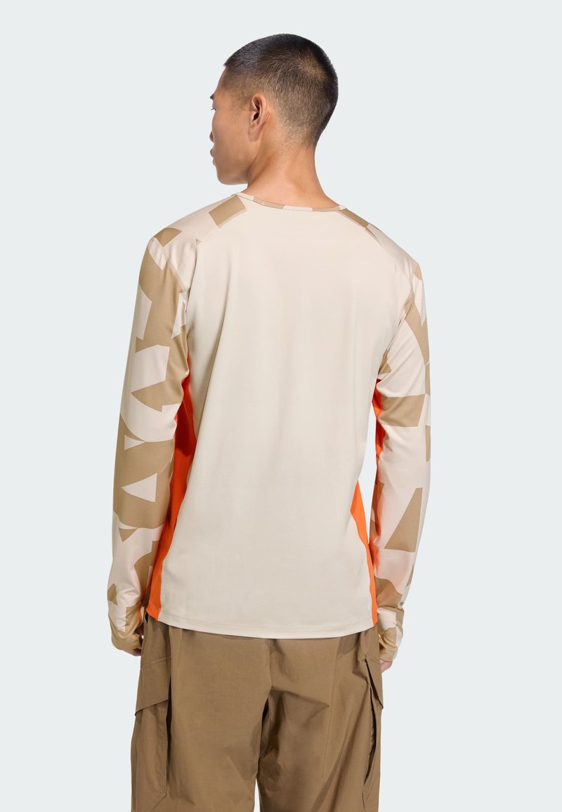 Camicia a maniche lunghe beige e arancione con motivi geometrici sulle maniche. Realizzata in tessuto morbido, presenta un colletto rotondo e una vestibilità aderente.