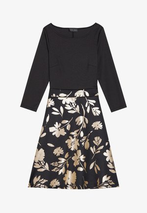 Zwarte jurk met lange mouwen, met een getailleerde bovenkant en een uitlopende rok versierd met gouden bloemmotieven. Soepele textuur, ronde halslijn.