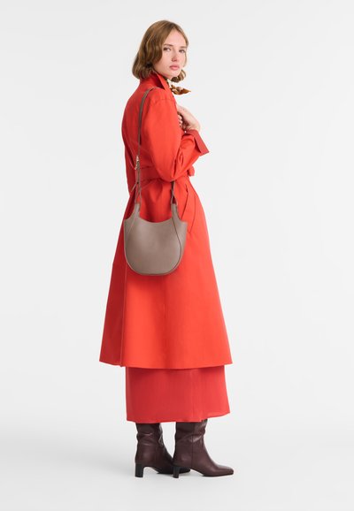 Roter Trenchcoat über einem passenden Rock, kombiniert mit braunen kniehohen Stiefeln und einer beigen Umhängetasche. Glatte Texturen, modernes Design.