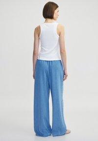Weißes ärmelloses Tanktop und hoch sitzende, locker sitzende hellblaue Jeanshose. Glattes Material mit entspannter Passform.