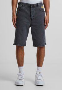 Dunkelgraue Denim-Shorts mit gerader Passform, ausgestattet mit Gürtelschlaufen, fünf Taschen und einem bunten Markenlogo auf der linken Vorderseite der Tasche.