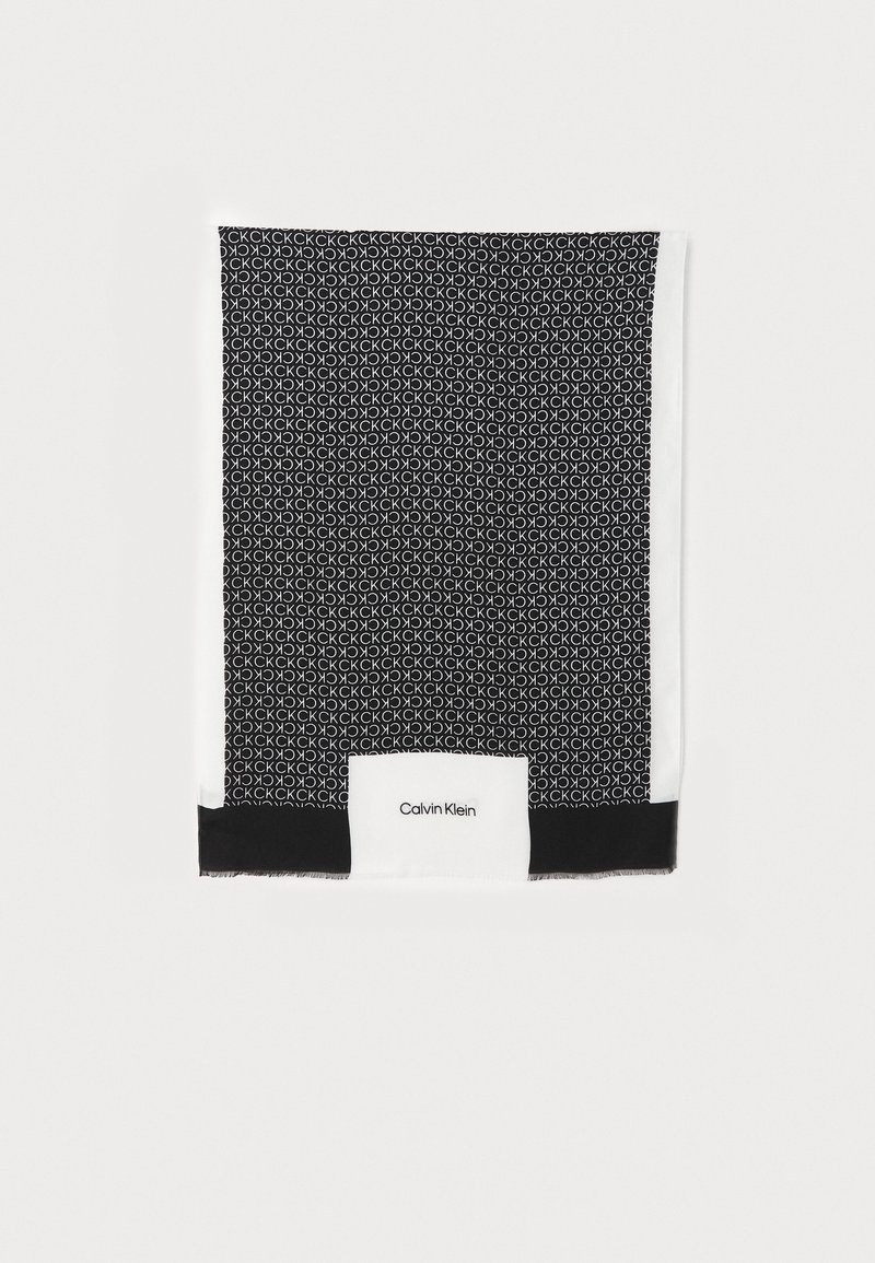 Écharpe noir et blanc avec motif répétitif du logo CK et texte Calvin Klein sur un panneau de fond blanc près de la fin.