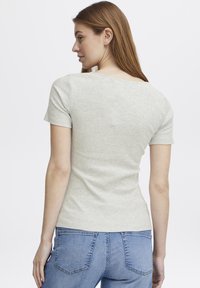 Lys grå ribbet t-shirt med korte �ærmer og rund halsudskæring, parret med blå jeans, set fra ryggen.