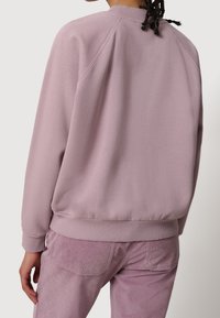 Sudadera rosa claro con cuello redondo y puños de canalé, con una textura suave y mangas raglán. Combinada con pantalones de pana a juego.