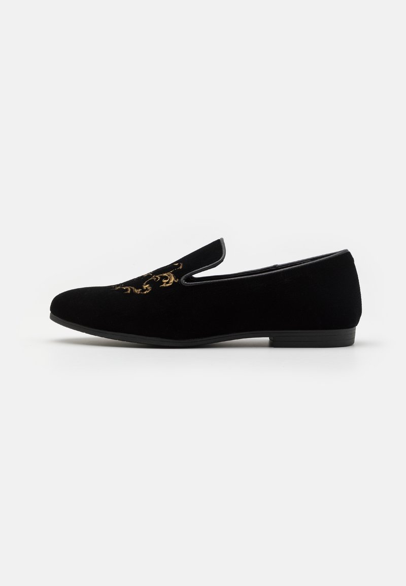 Mocassin en velours noir sans lacets avec broderie dorée sur le dessus et petit talon plat, vu de côté sur fond blanc.