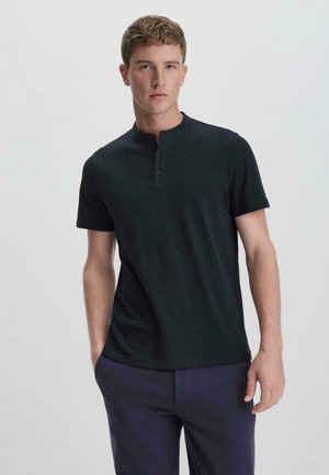 Maglietta henley nera a maniche corte in morbido cotone, con scollatura rotonda e pattina a due bottoni, abbinata a pantaloni blu scuro.