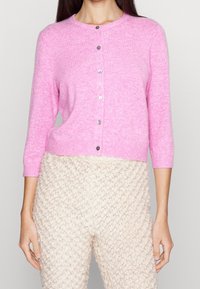Fuksia napitettava kardigan, jossa on kolmannes hihoista, neulepinta ja pyöreä pääntie; edessä hopeiset napit.