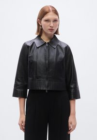 Μαύρο cropped δερ�μάτινο μπουφάν με γιακά, εμπρόσθιο φερμουάρ και ραβδωτή υφή στο τελείωμα και τα μανίκια. Μινιμαλιστικός σχεδιασμός με πλαϊνές τσέπες.