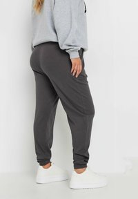 Donkergrijze geribde joggingbroek met opgerolde enkels, gecombineerd met een lichtgrijze oversized sweatshirt en witte sneakers. Eenvoudig ontwerp en textuurstof.