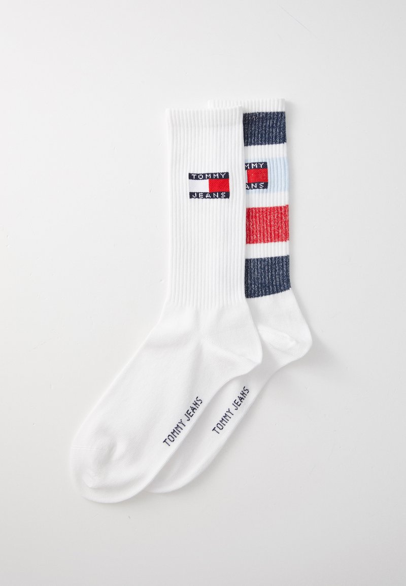 Chaussettes blanches longues jusqu'aux chevilles avec un design en côtes. Une chaussette présente un motif de rayures colorées ; les deux affichent le logo "TOMMY JEANS".