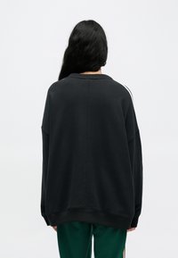 Čierna oversize mikina s voľným strihom, rebrovaným výstrihom a kontrastnými bielymi pruhmi na ramenách. Mäkká bavlnená textúra.