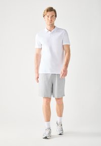 Biała koszulka polo zestawiona z jasnoszarymi szortami. Model ubrany w szare sneakersy i białe skarpetki, stojący na neutralnym tle.