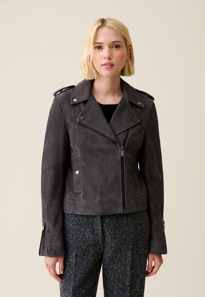 Giacca in suede grigia con colletto a scollo a V, chiusura frontale con zip e tasche laterali. Presenta spalline e polsini con zip per un tocco di stile in più.