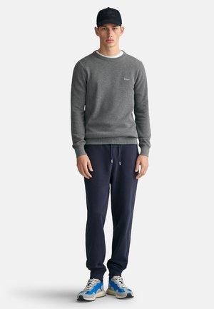 Gray sweatshirt with round neckline, navy sweatpants, and blue-accented sneakers. Model wears a matching dark cap. Simple, casual design.