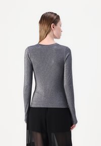 Long-sleeve shirt in metallic gray fabric. Fitted design with a round neckline and smooth texture, worn with black sheer pants.