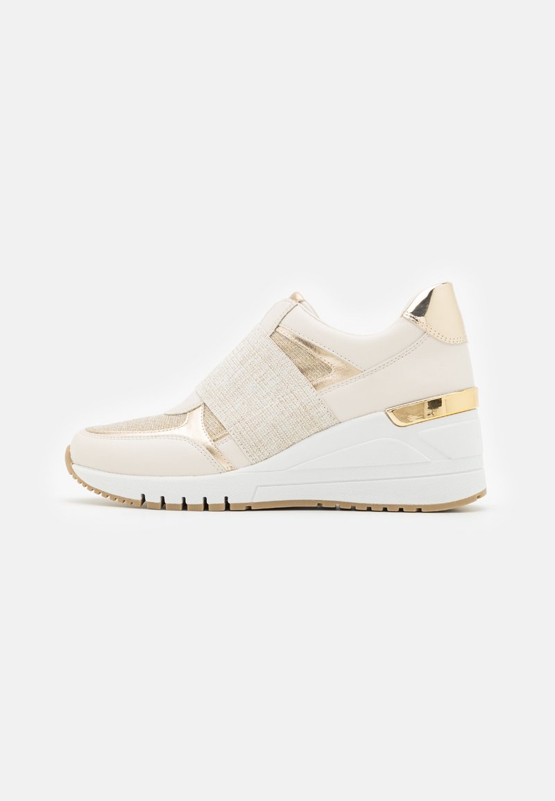 Baskets compensées en beige clair avec des accents dorés métalliques. Elles présentent un dessus texturé, des bandes élastiques et une semelle en caoutchouc blanc avec une traction marron.