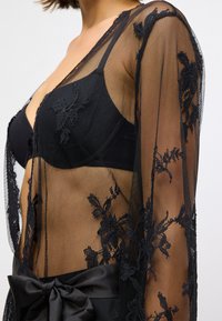 Svart mesh kimono med blomstermønster, åpen design og satengliv med sløyfe. Gjennomsiktig tekstur fremhever lagdelte plagg under.