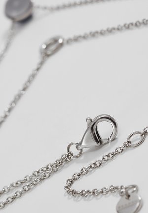 Close-up van een zilverkleurige karabijnsluiting bevestigd aan een fijne kettingketting op een witte ondergrond.