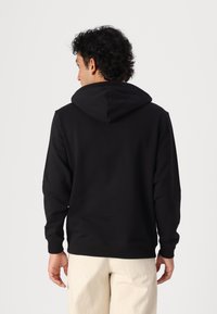 Haut à capuche noir avec une texture en tissu, présentant une capuche et des manches longues. Le design inclut des poignets et une taille côtelés. Vue arrière montrée.