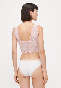 Lace bralette i myk rosa med bølgemønstrede kanter, parret med hvite truser med blonder. Har en ryggløs design og delikat tekstur.