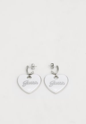 Hartvormige oorbellen van witte kunststof met zilveren hardware. Bevat "Guess" in grijze letters. Glad oppervlak en gepolijste afwerking.