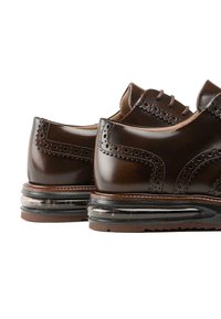 Chaussures en cuir marron avec des détails en brogue, dotées d'une semelle transparente à coussin d'air. Fini lisse, bout rond et design à lacets.