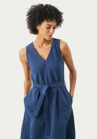 Navyblauw mouwloos jurkje met V-hals, textuurstof, tailleband en zijzakken, met een ontspannen pasvorm en vloeiende silhouet.