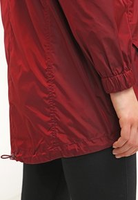 Czerwona, lekka kurtka wykonana z błyszczącego materiału, z elastycznymi mankietami, ściągaczem w dolnej części i luźnym krojem. Brak widocznych znaków towarowych i wzorów.