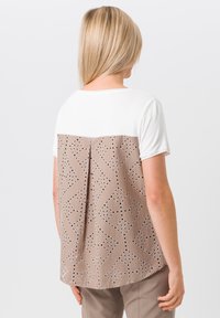 Korte mouw top met een witte voorkant en een beige patroon achterkant, voorzien van uitgesneden ontwerpen en een ontspannen pasvorm. Soepele textuur en afgeronde zoom.